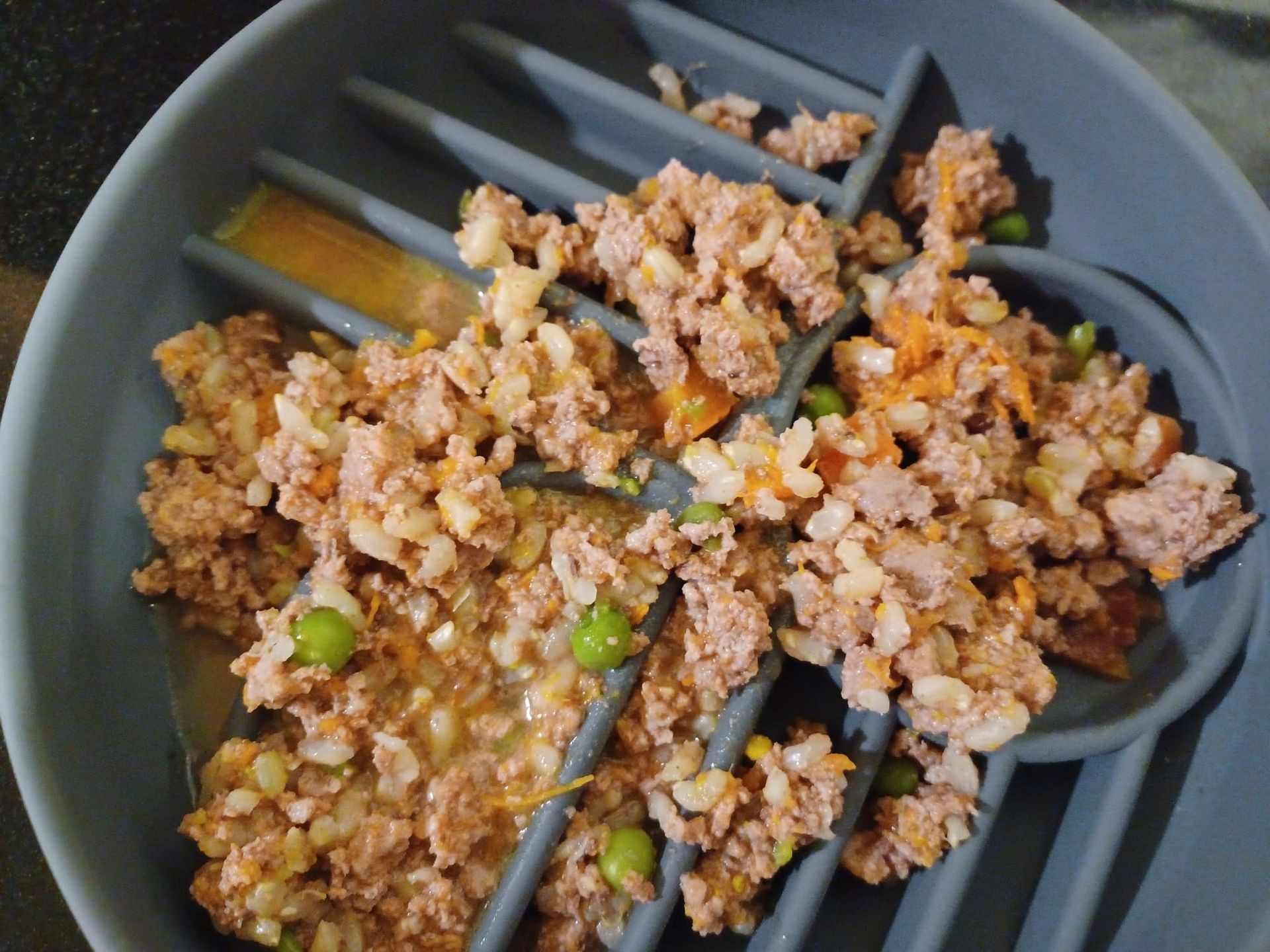 Cooked ground meat with peas and rice served in a gray pet food bowl with ridges.